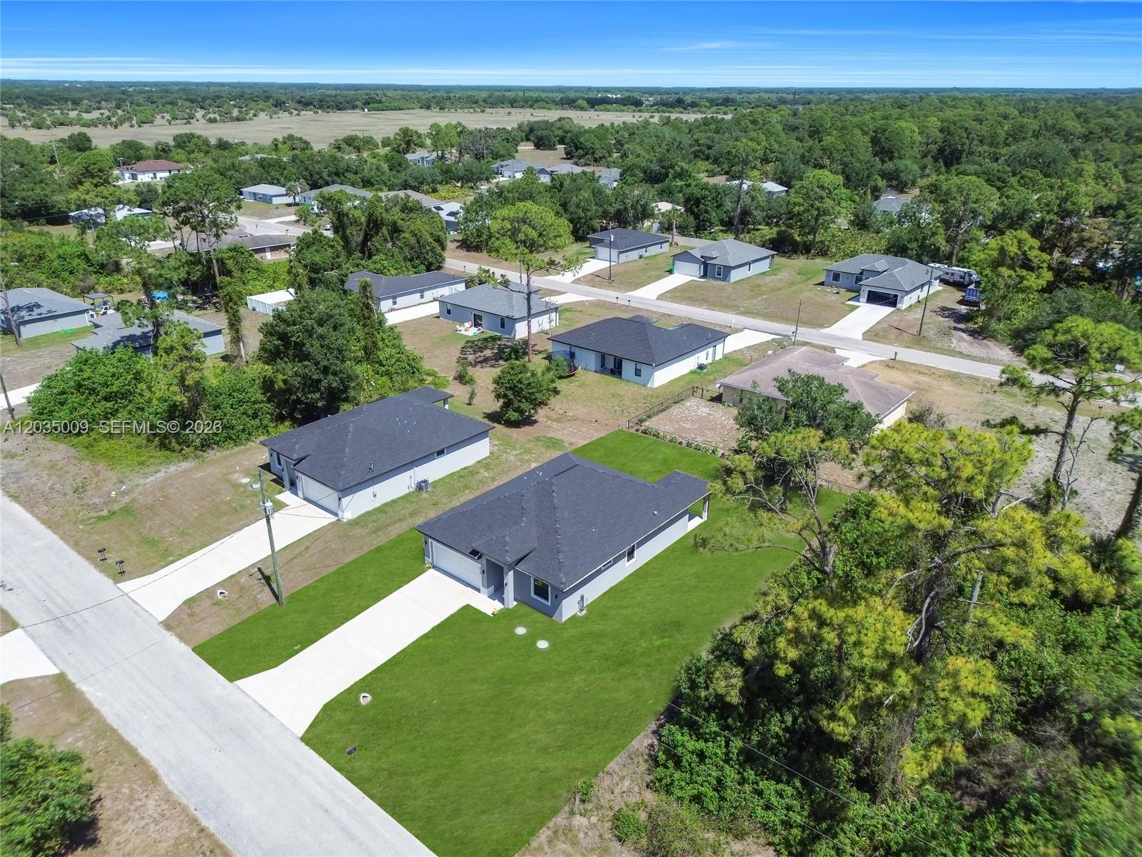 An aerial view shows several single-story houses with dark roofs situated in a wooded neighborhood — 6210 Forest Court, La Belle FL 33935, LA BELLE, FL