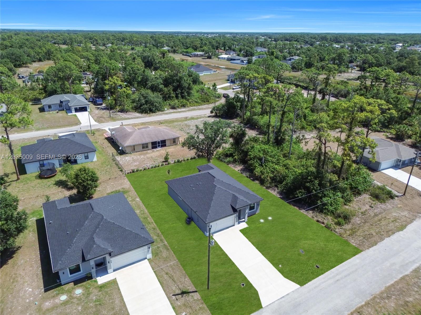 An aerial view shows several single-story houses with dark roofs situated in a wooded area — 6210 Forest Court, La Belle FL 33935, LA BELLE, FL