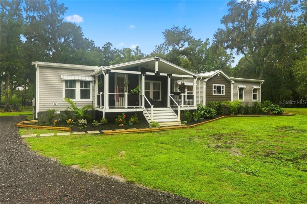 A single-story house with light gray siding, a dark porch, and a gravel driveway — 22256 CHERATON ROAD, BROOKSVILLE, FL