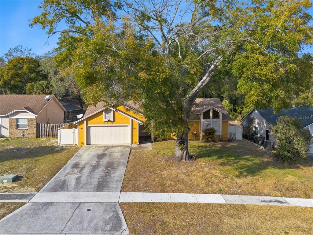 A yellow single-story house with a two-car garage and a large tree in the yard — 6815 CRESCENT RIDGE ROAD, ORLANDO, FL