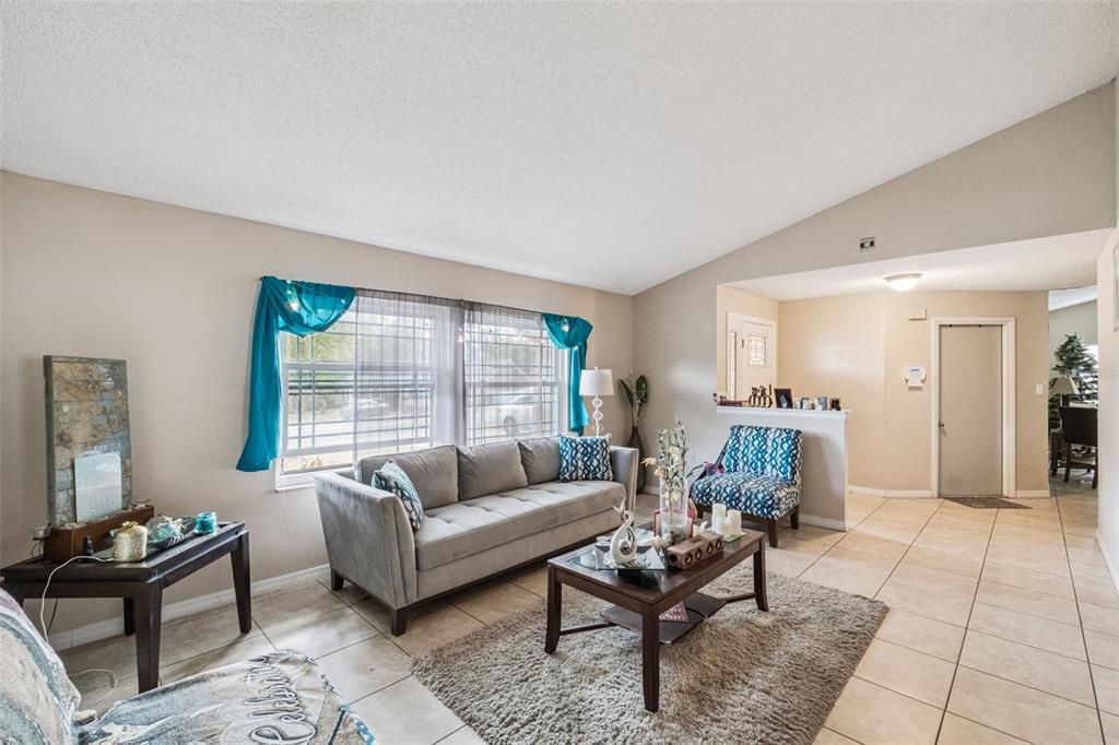 A living room features a gray sofa, a patterned armchair, and tile flooring — 6815 CRESCENT RIDGE ROAD, ORLANDO, FL