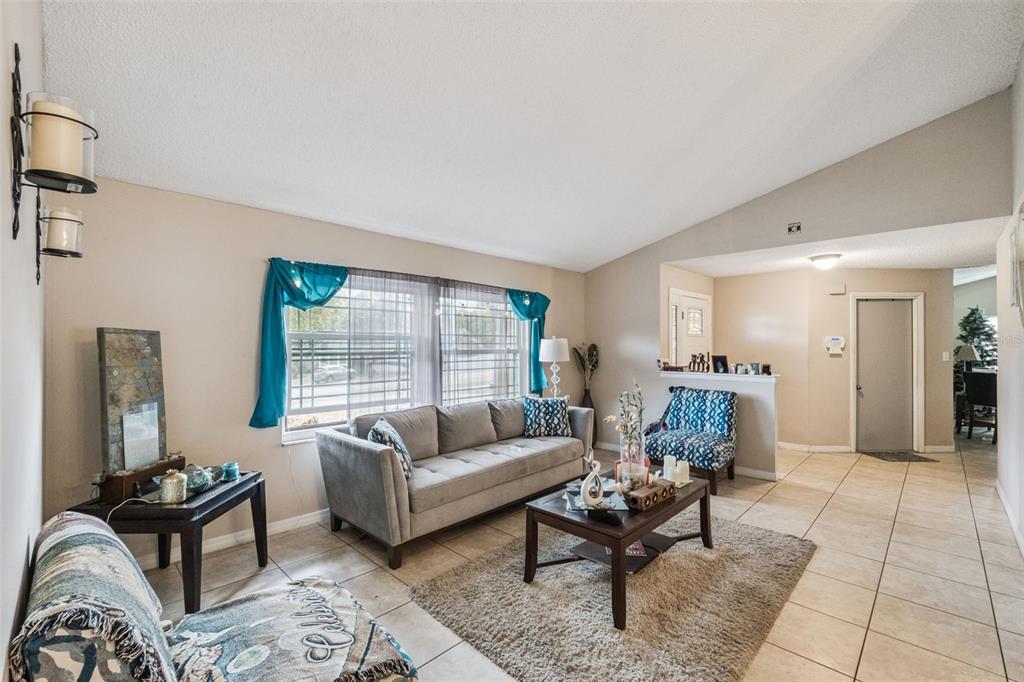 A living room features a gray sofa, a coffee table, and tile flooring under vaulted ceilings — 6815 CRESCENT RIDGE ROAD, ORLANDO, FL