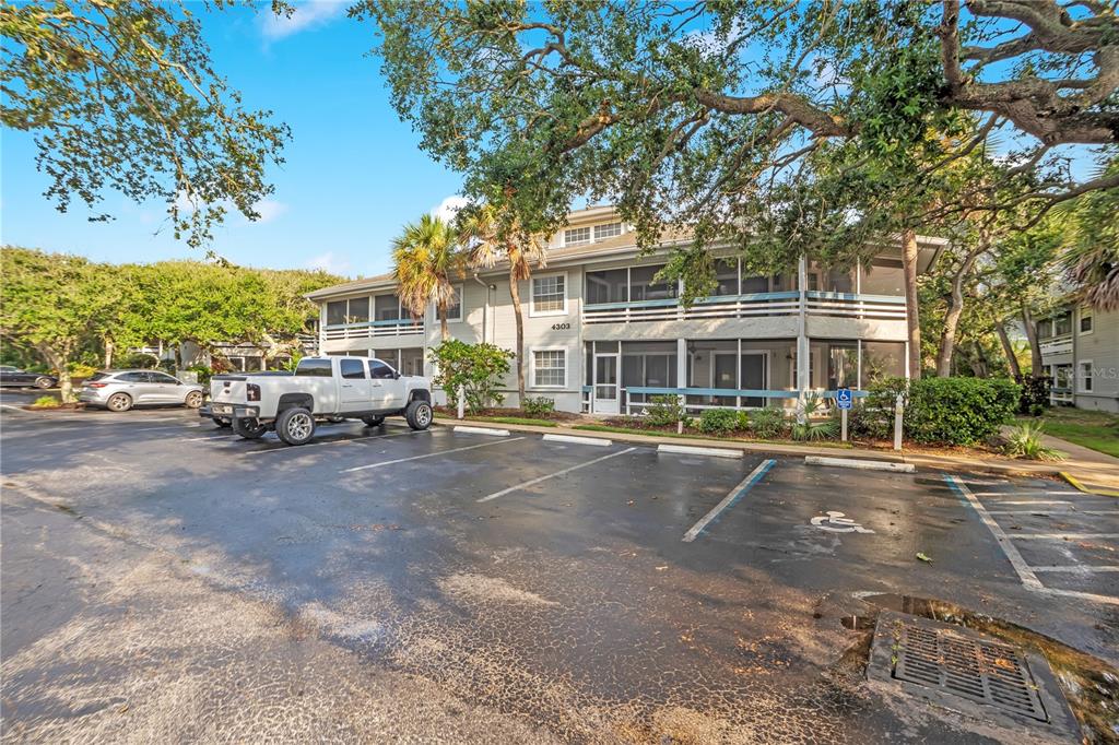 A two-story apartment building with screened balconies sits behind a parking lot with accessible spaces — 4303 SEA MIST DRIVE UNIT 224, NEW SMYRNA BEACH, FL