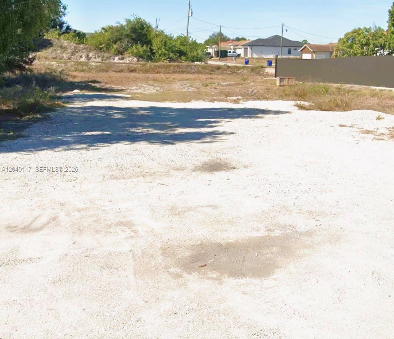 A vacant, unpaved lot features sparse vegetation and a brown privacy fence in the background — 2908 Donald Ave S, Lehigh Acres FL 33976, LEHIGH ACRES, FL