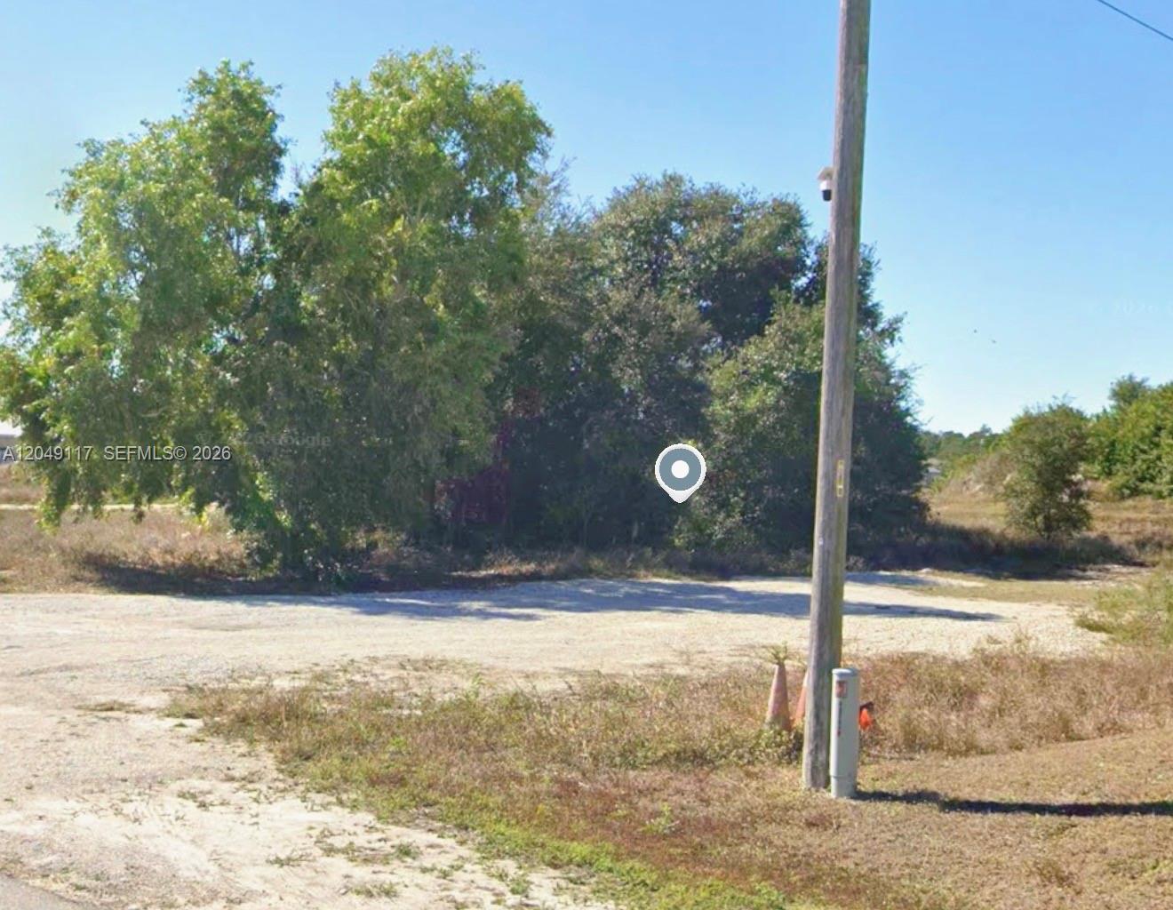 A dirt lot with trees and a utility pole under a clear blue sky — 2908 Donald Ave S, Lehigh Acres FL 33976, LEHIGH ACRES, FL