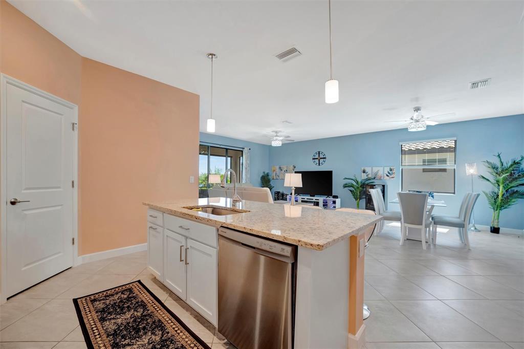 A kitchen island with a stainless steel dishwasher faces an open-concept living and dining area — 5317 CORAL REEF WAY, BRADENTON, FL