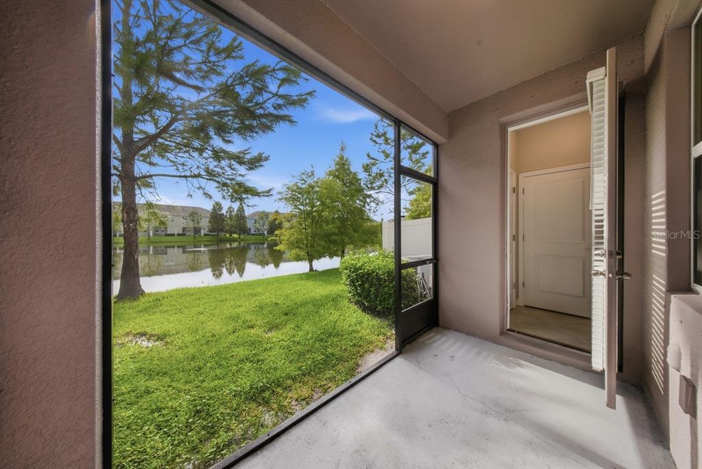 A screened-in patio overlooks a grassy lawn and a small pond with trees — 18836 NOBLE CASPIAN DRIVE, LUTZ, FL