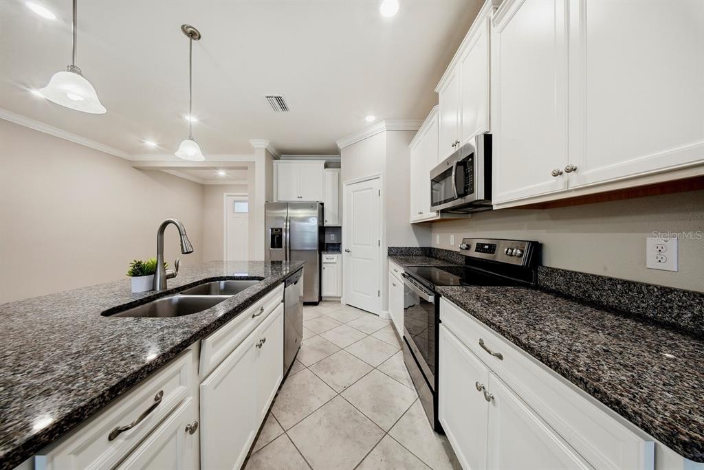 A kitchen features white cabinets, granite countertops, stainless steel appliances, and a central island sink — 18836 NOBLE CASPIAN DRIVE, LUTZ, FL