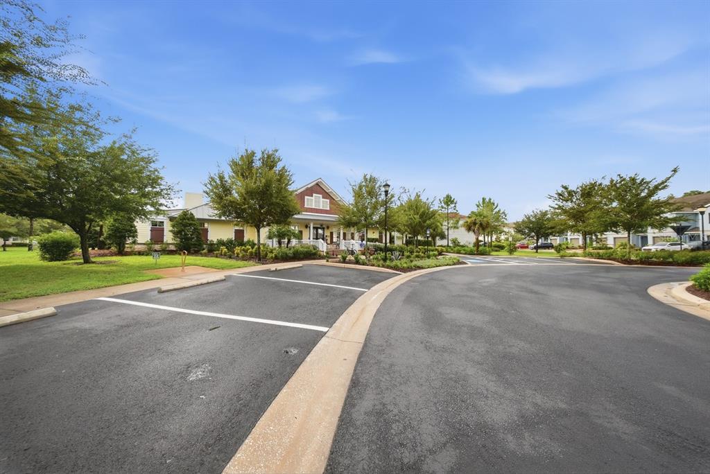 A paved parking lot sits in front of a community clubhouse surrounded by green trees — 18836 NOBLE CASPIAN DRIVE, LUTZ, FL