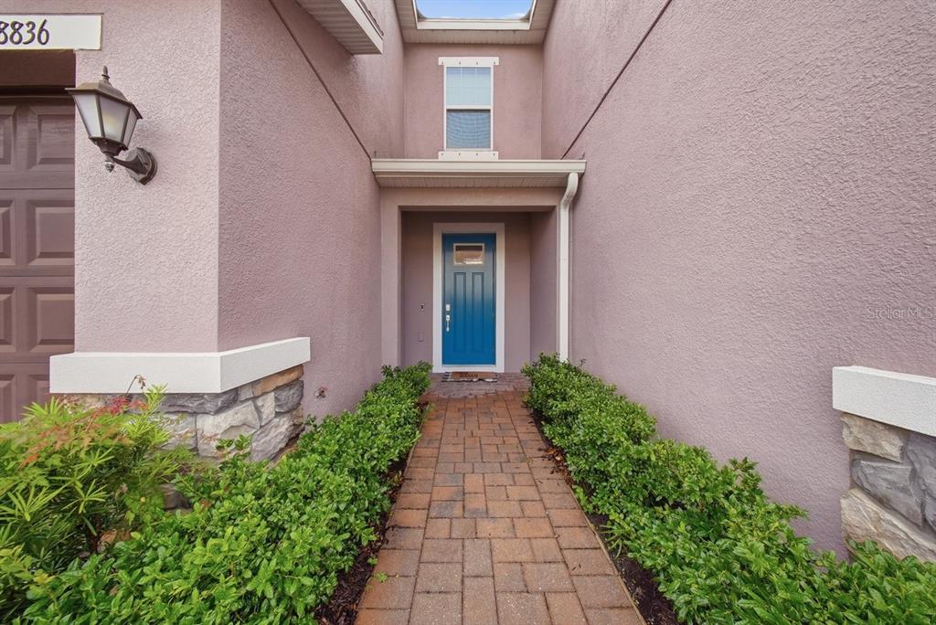 A brick walkway leads to a blue front door flanked by hedges and stone accents — 18836 NOBLE CASPIAN DRIVE, LUTZ, FL