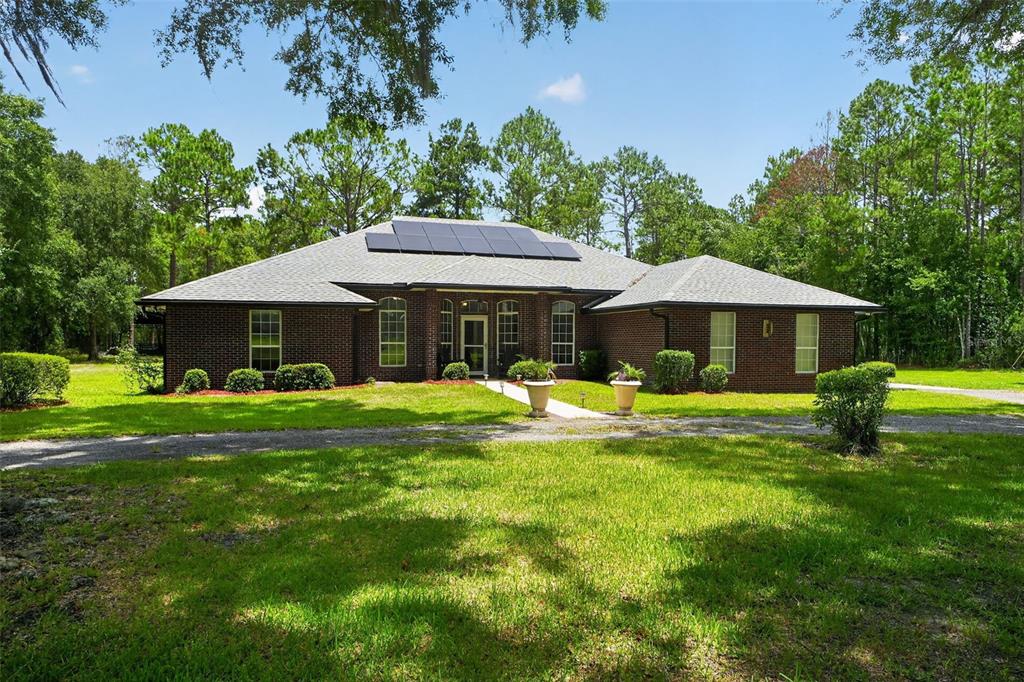A single-story brick house with a solar panel array on the roof and a lawn — 2527 NW COUNTY ROAD 225, LAWTEY, FL