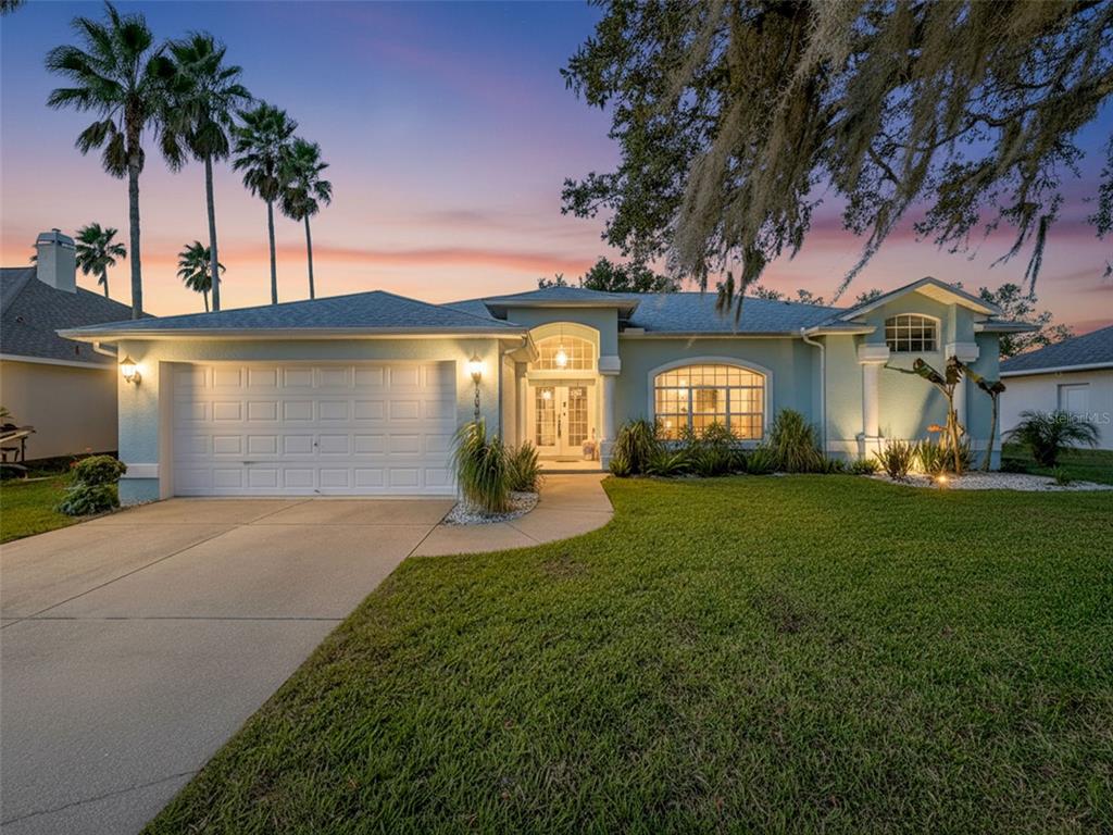 A single-story house with a two-car garage, arched entryway, and palm trees at sunset — 3365 INDIAN RIVER STREET, SPRING HILL, FL