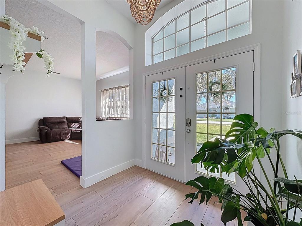 An entryway with light wood flooring, double glass-paneled doors, and an arched wall opening — 3365 INDIAN RIVER STREET, SPRING HILL, FL