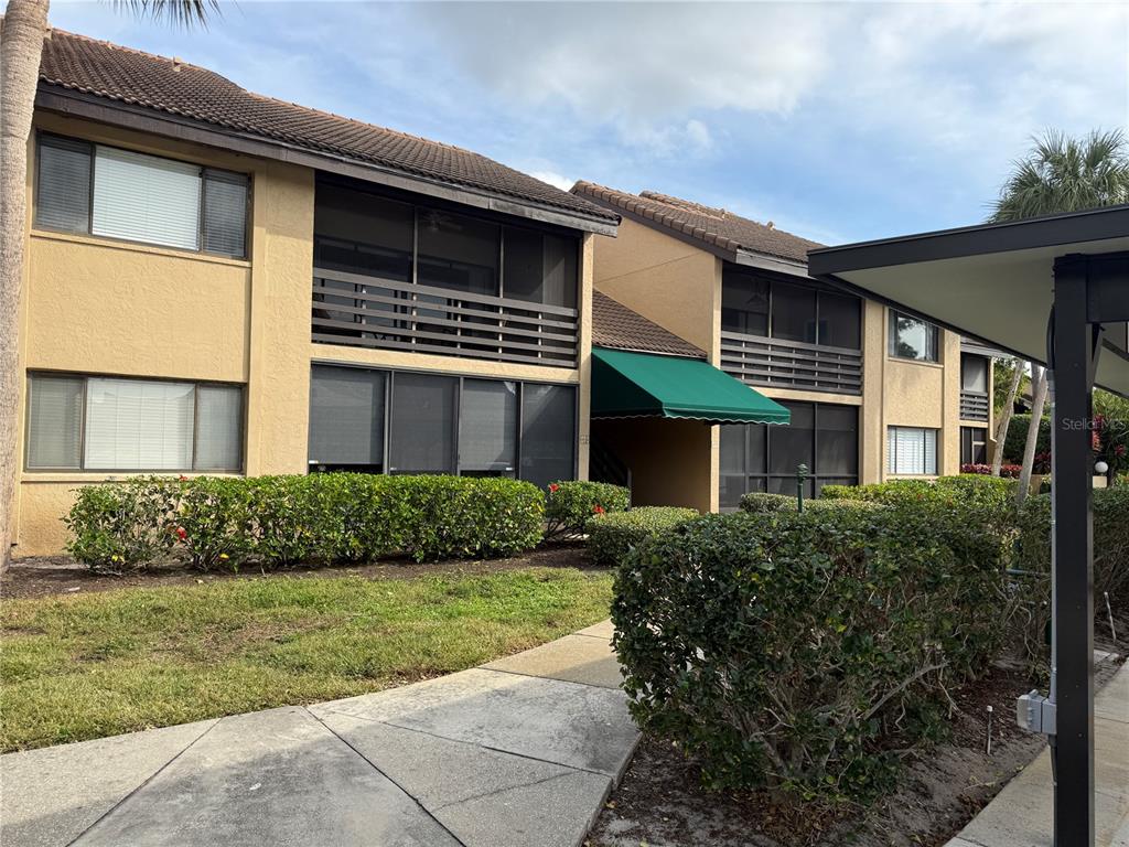 A two-story apartment building with tan stucco walls, screened balconies, and a green awning — 5631 ASHTON LAKE DRIVE UNIT 7, SARASOTA, FL