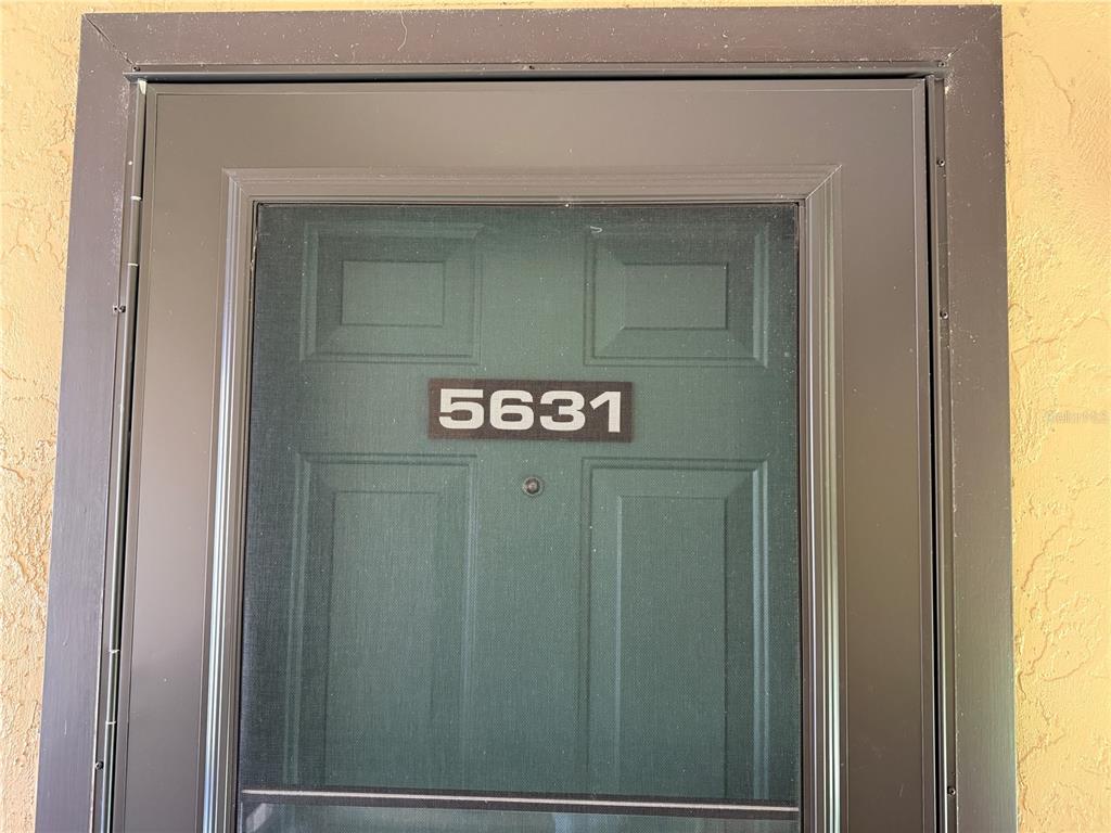 A dark green front door with a screen door and the house number 5631 — 5631 ASHTON LAKE DRIVE UNIT 7, SARASOTA, FL