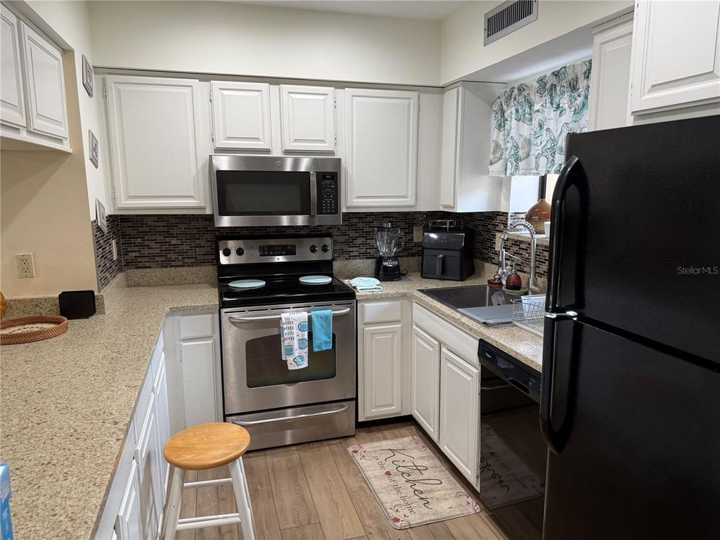 A kitchen features white cabinets, stainless steel appliances, a black refrigerator, and a tiled backsplash — 5631 ASHTON LAKE DRIVE UNIT 7, SARASOTA, FL
