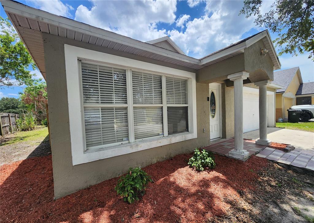 A tan stucco house exterior features a large front window, white columns, and red mulch — 5298 YAUPON STREET, ORLANDO, FL
