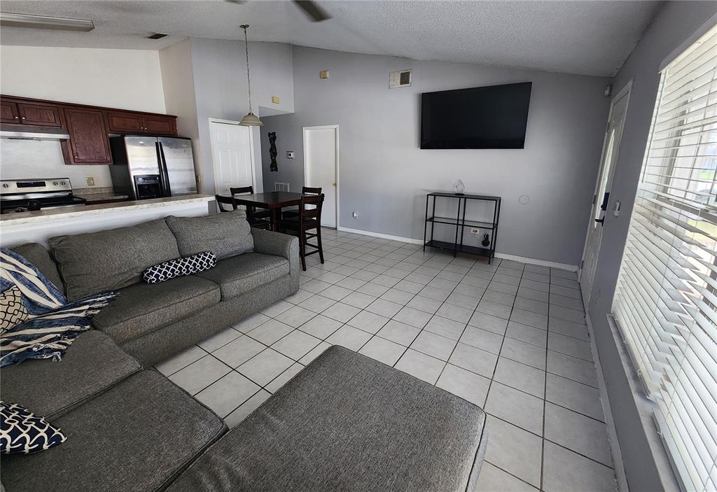 A living room with gray tile floors, a sectional sofa, and a wall-mounted television — 5298 YAUPON STREET, ORLANDO, FL