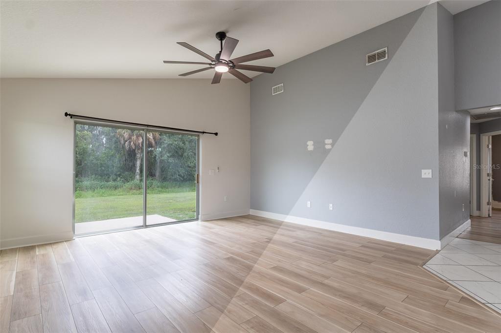 A living room features light wood-look flooring, a vaulted ceiling, a ceiling fan, and sliding doors — 344 KISSENGEN PARK DRIVE, BARTOW, FL