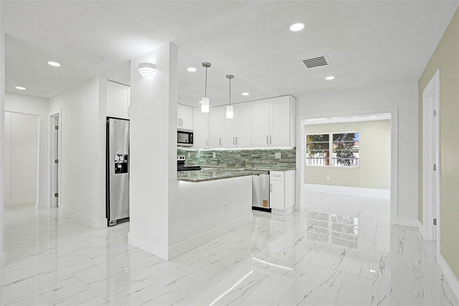 A modern kitchen features white cabinets, marble-patterned tile floors, and a granite-topped peninsula — 1437 SW 1st Avenue, Deerfield Beach FL 33441, DEERFIELD BEACH, FL