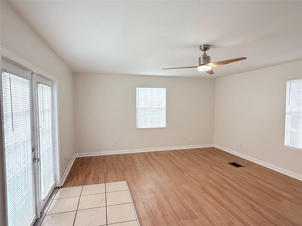 An empty room features light wood-look flooring, a ceiling fan, white walls, and glass doors — 3611 2ND AVENUE S, ST PETERSBURG, FL