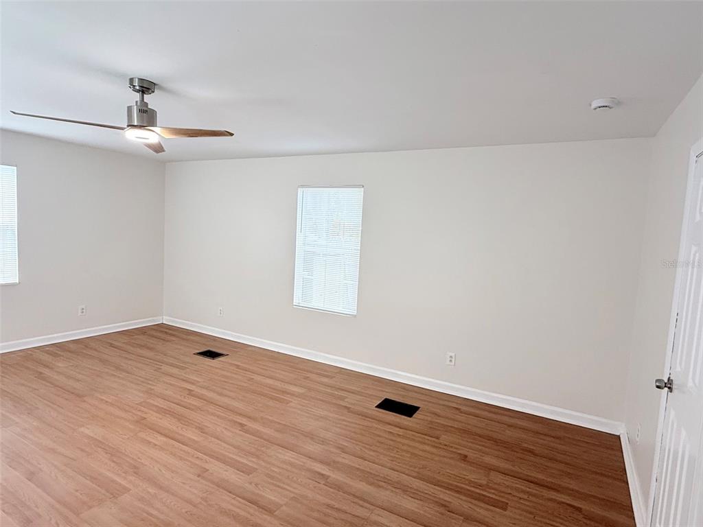 An empty room features light-colored walls, wood-look flooring, a ceiling fan, and two floor vents — 3611 2ND AVENUE S, ST PETERSBURG, FL