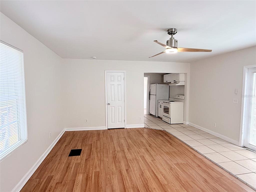 A living room with wood-look flooring features a ceiling fan, a white door, and tiled kitchen — 3611 2ND AVENUE S, ST PETERSBURG, FL