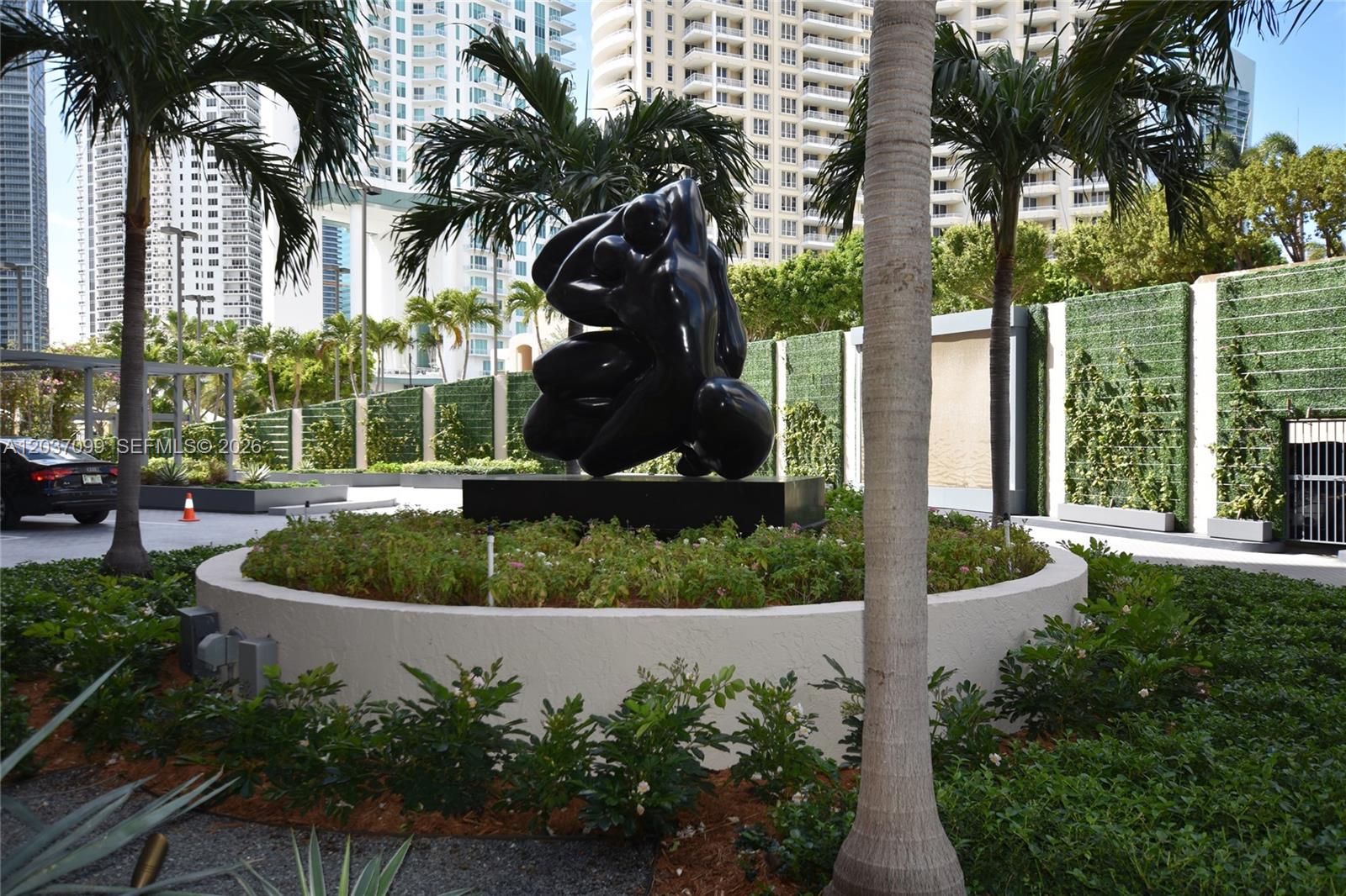 A black abstract sculpture sits in a circular garden bed surrounded by palm trees — 540 Brickell Key Dr # 1513, Miami FL 33131, MIAMI, FL