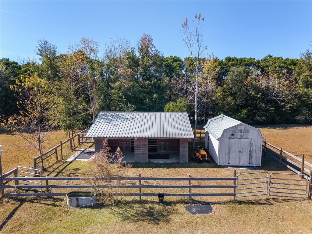 An aerial view shows a wooden barn and a white shed inside a fenced pasture — 9128 NW 238TH STREET, ALACHUA, FL