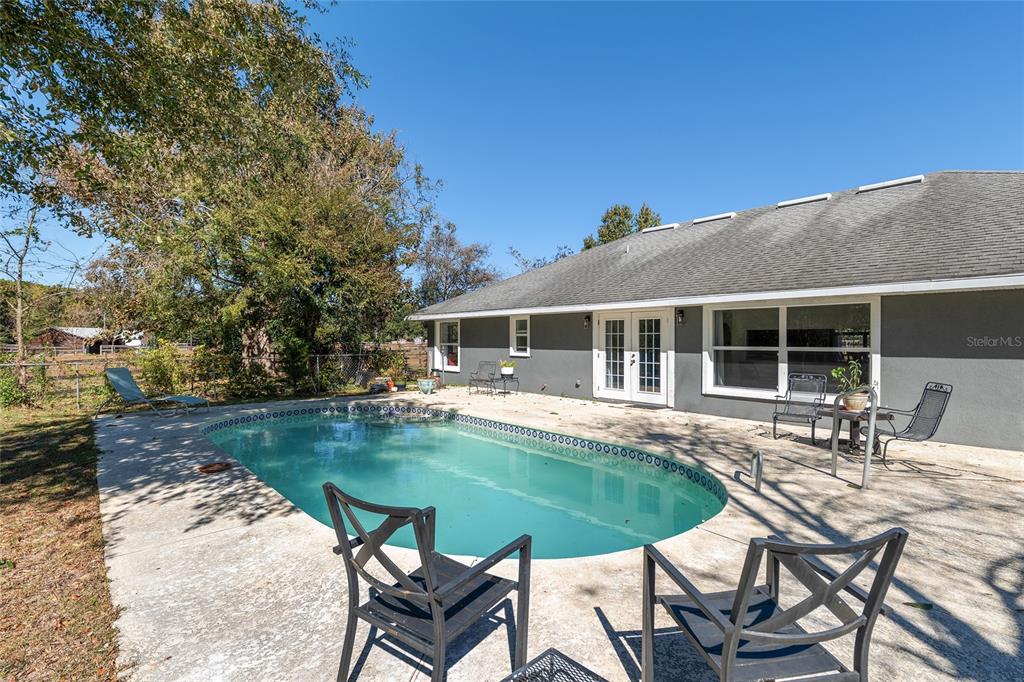A backyard features a swimming pool, concrete patio, and a gray house with French doors — 9128 NW 238TH STREET, ALACHUA, FL