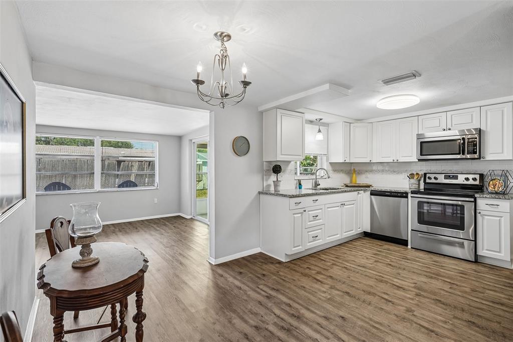 A kitchen with white cabinets and stainless steel appliances opens into a dining area — 7215 MAYFIELD DRIVE, PORT RICHEY, FL