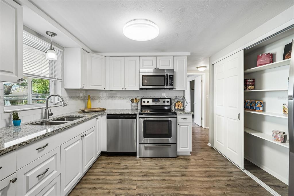 A kitchen with white cabinets, stainless steel appliances, granite countertops, and a sliding door pantry — 7215 MAYFIELD DRIVE, PORT RICHEY, FL