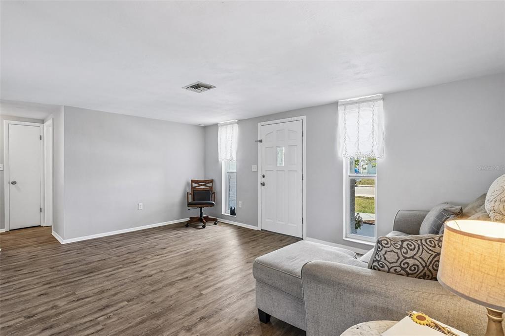 A living room features light gray walls, wood-look flooring, a front door, and a sectional sofa — 7215 MAYFIELD DRIVE, PORT RICHEY, FL