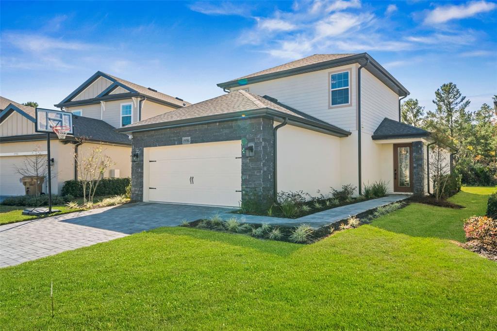A two-story house with a stone-accented garage, beige siding, and a paved driveway — 7796 SOMERSWORTH DRIVE, KISSIMMEE, FL