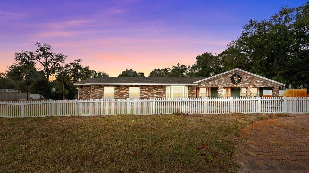 A single-story brick house with a white picket fence and a paved driveway at sunset — 746 W WASHINGTON AVENUE W, LAKE HELEN, FL