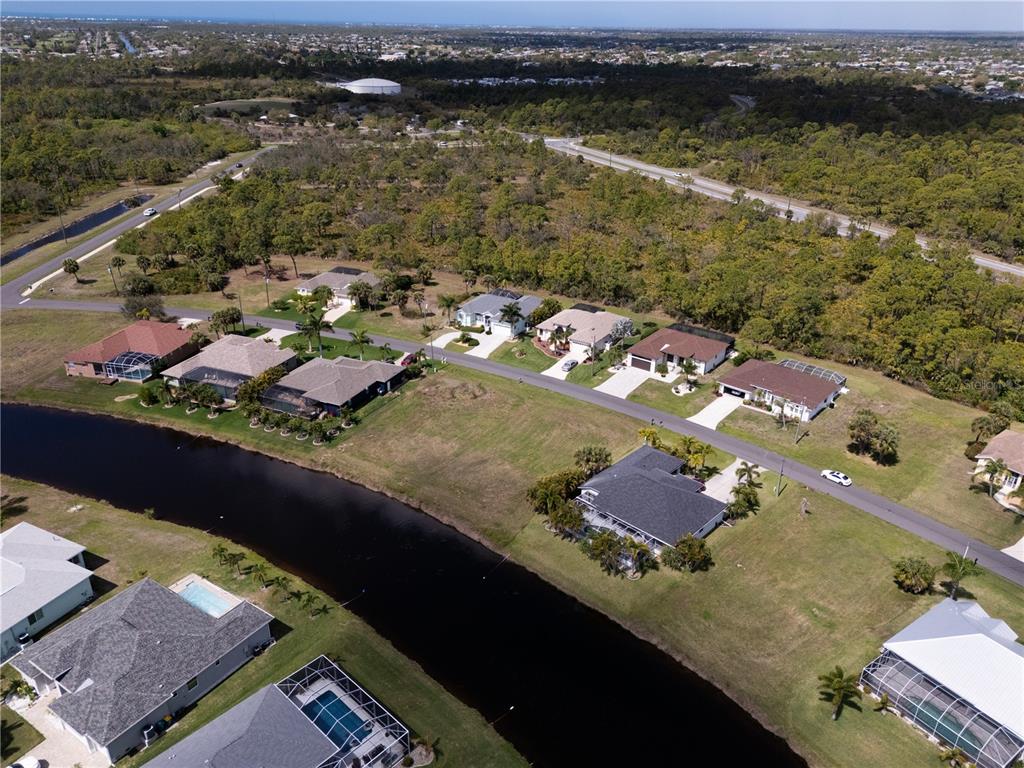 An aerial view shows a suburban neighborhood with houses, a canal, and surrounding wooded areas — 134 WHITE MARSH LANE, ROTONDA WEST, FL
