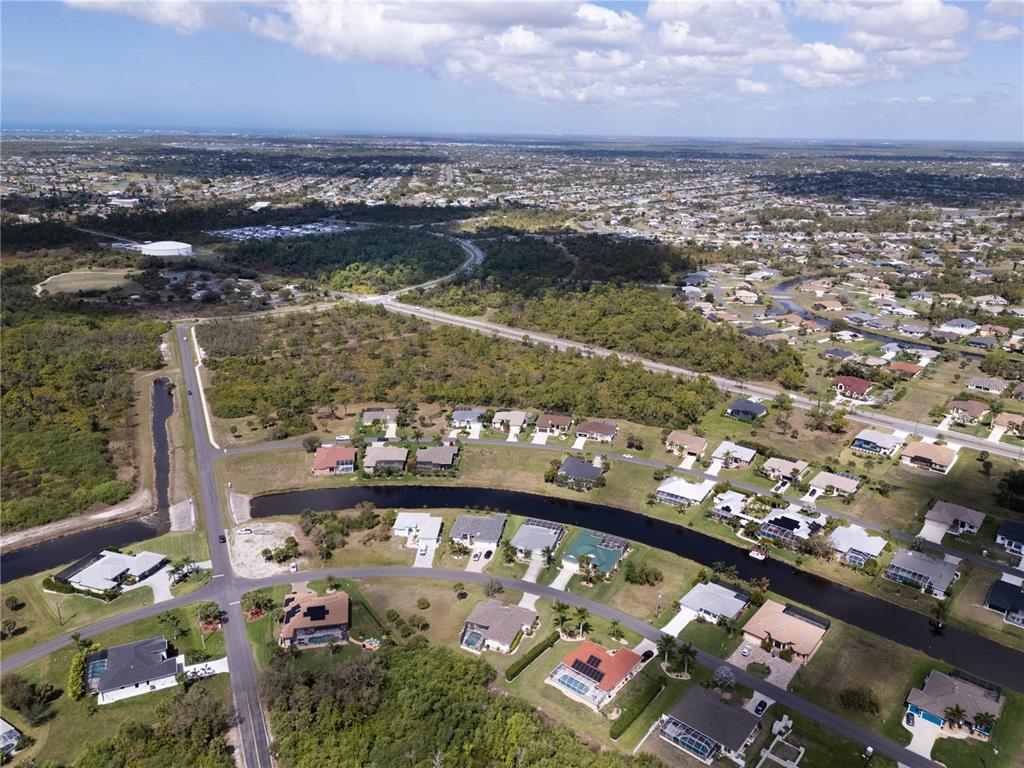 Aerial view of a suburban neighborhood featuring single-family homes, a canal, and surrounding wooded areas — 134 WHITE MARSH LANE, ROTONDA WEST, FL
