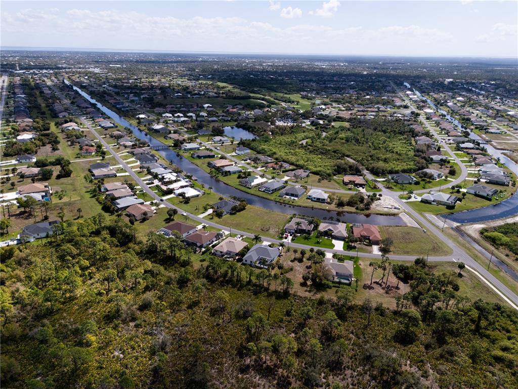 An aerial view shows a suburban neighborhood with houses lining a canal and surrounding vegetation — 134 WHITE MARSH LANE, ROTONDA WEST, FL