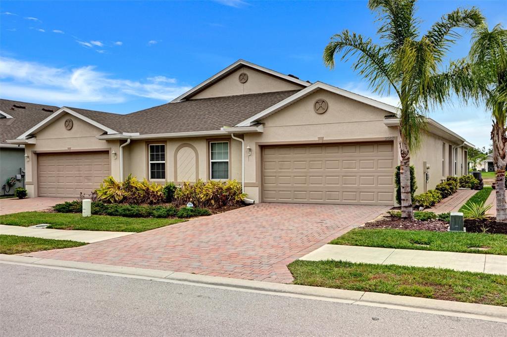 A tan duplex home with two garages, a brick paver driveway, and palm trees — 20462 PLUMWOOD LOOP, NORTH FORT MYERS, FL