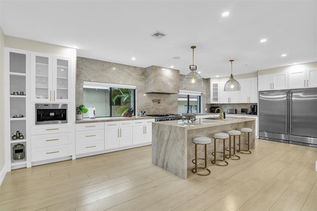 A modern kitchen features white cabinetry, a large stone island, and stainless steel appliances — 319 S Riverside Drive, Pompano Beach FL 33062, POMPANO BEACH, FL