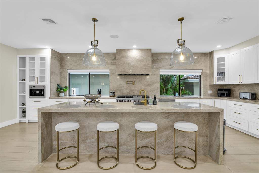 A modern kitchen features a large stone island with four stools and matching marble backsplash — 319 S Riverside Drive, Pompano Beach FL 33062, POMPANO BEACH, FL
