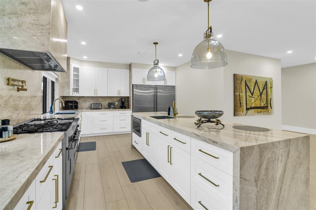 A modern kitchen features white cabinetry, stone countertops, stainless steel appliances, and two pendant lights — 319 S Riverside Drive, Pompano Beach FL 33062, POMPANO BEACH, FL