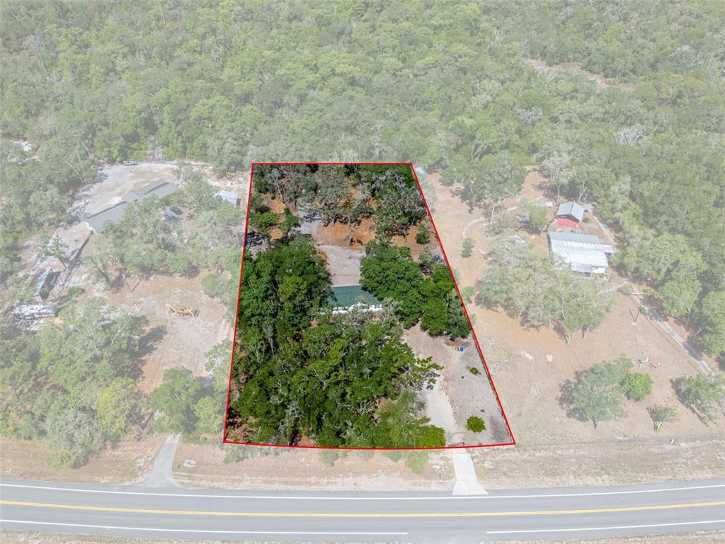 An aerial view shows a house nestled within a wooded lot outlined in red — 4059 MCKETHAN ROAD, DADE CITY, FL