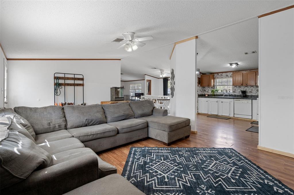 A living room with a gray sectional sofa and a patterned rug leads into a kitchen — 4059 MCKETHAN ROAD, DADE CITY, FL