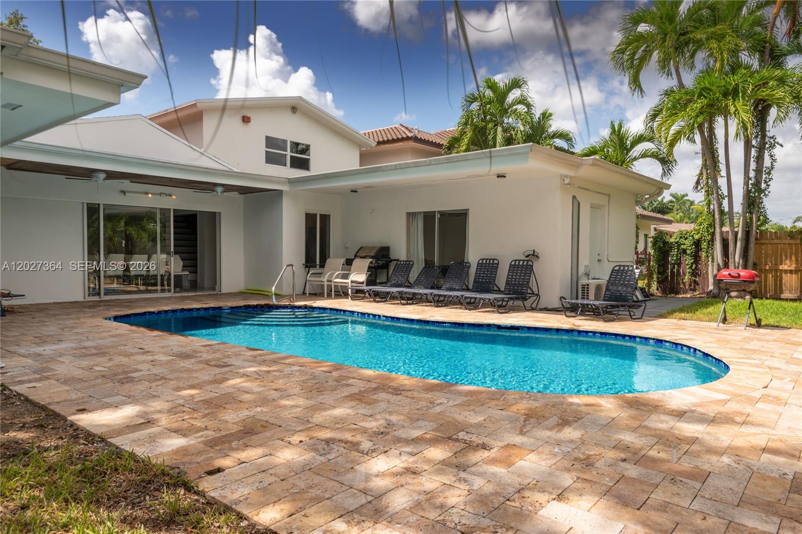 A backyard features a swimming pool, stone patio, lounge chairs, and a red charcoal grill — 2555 NE 202nd St, Miami FL 33180, MIAMI, FL
