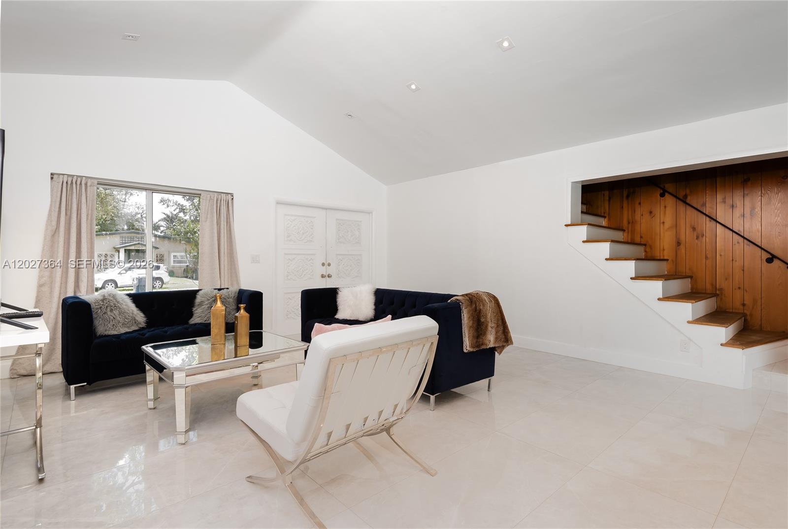 A living room features white vaulted ceilings, tiled floors, dark blue sofas, and wooden stairs — 2555 NE 202nd St, Miami FL 33180, MIAMI, FL