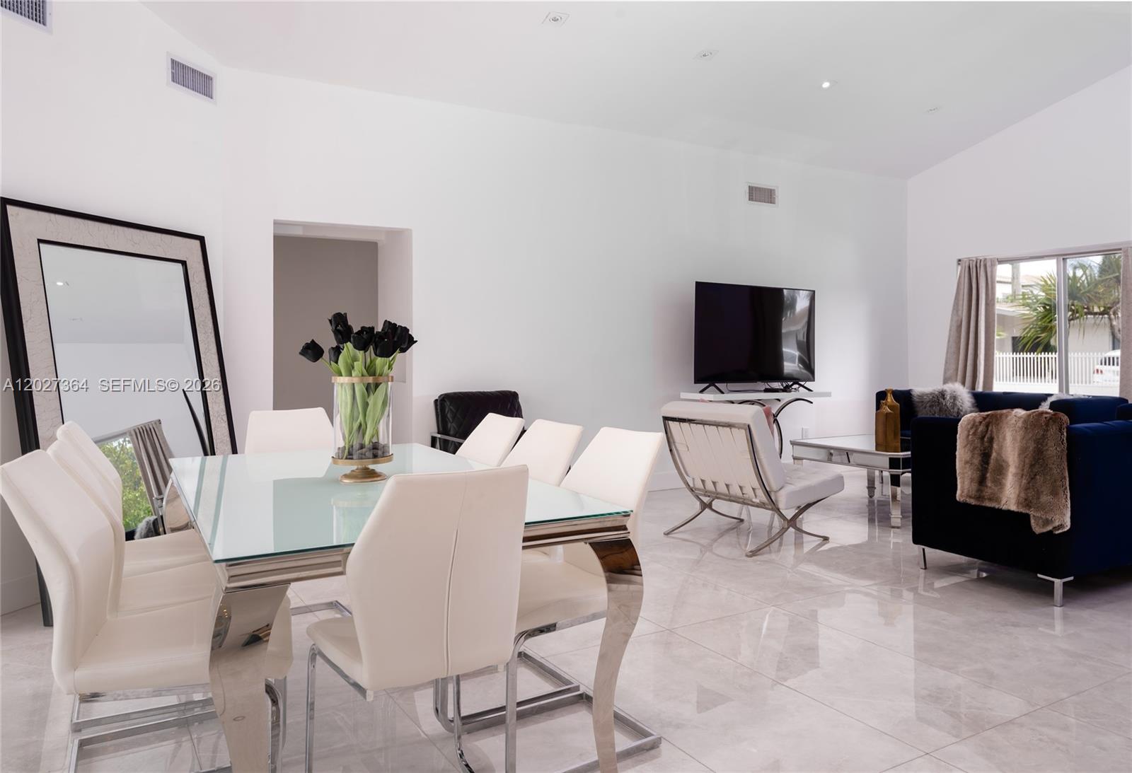 A modern dining and living area features white tile floors, a glass table, and white chairs — 2555 NE 202nd St, Miami FL 33180, MIAMI, FL