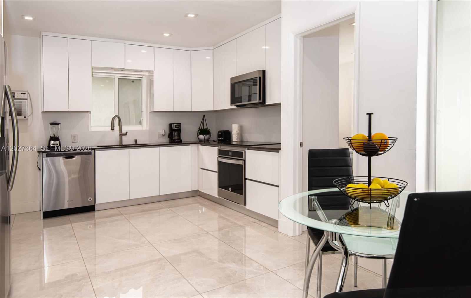A modern kitchen features white cabinets, stainless steel appliances, and a glass dining table — 2555 NE 202nd St, Miami FL 33180, MIAMI, FL