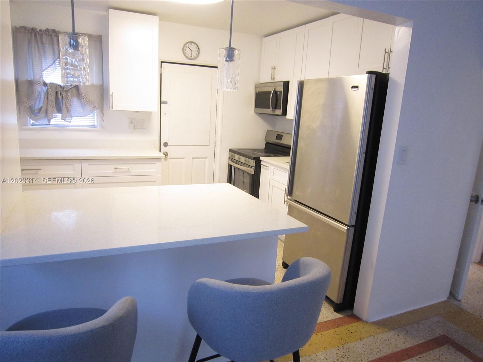 A kitchen features white cabinets, stainless steel appliances, a quartz island, and two blue chairs — 522 N 19th Ave # 5, Hollywood FL 33020, HOLLYWOOD, FL