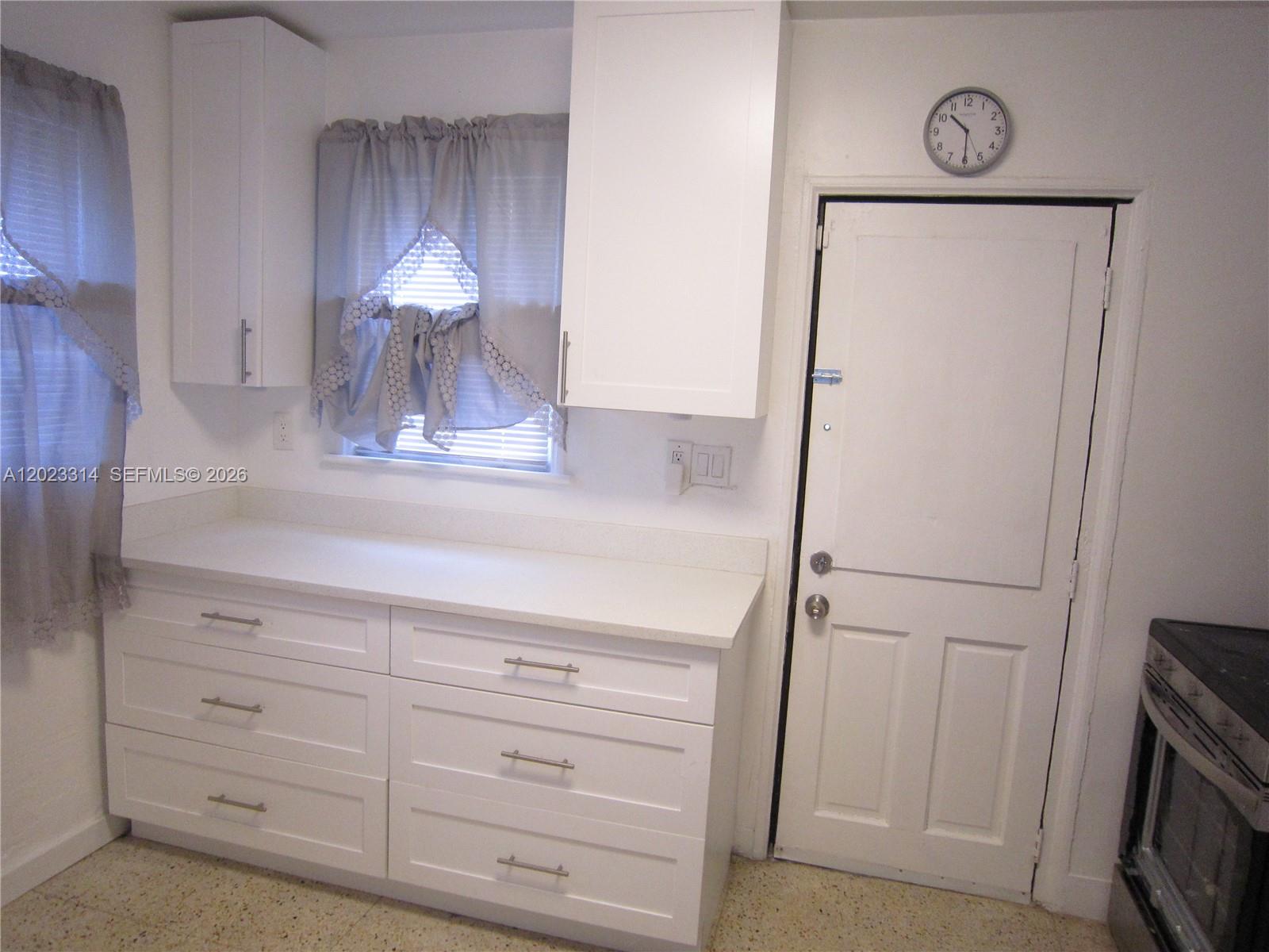 A kitchen features white cabinets, a countertop, a window with curtains, and a door — 522 N 19th Ave # 5, Hollywood FL 33020, HOLLYWOOD, FL